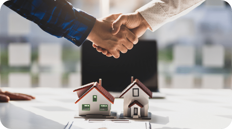 Two realtors shaking hands over mini model homes in a brokers office Full Heart Rentals Property Management Company in Panama City & Panama City Beach for renters & owners
